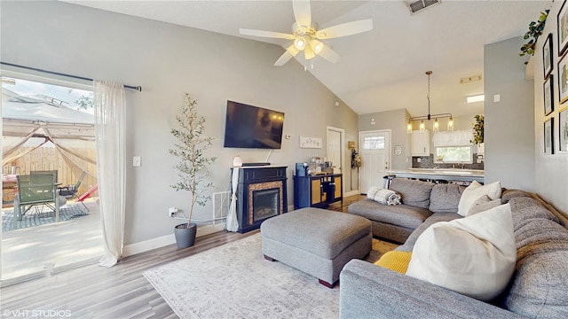 living room featuring baseboards, a glass covered fireplace, visible vents, ceiling fan with notable chandelier, and light wood-style floors