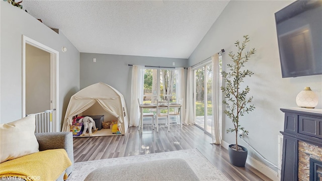 interior space with a textured ceiling, a stone fireplace, access to outside, vaulted ceiling, and wood finished floors