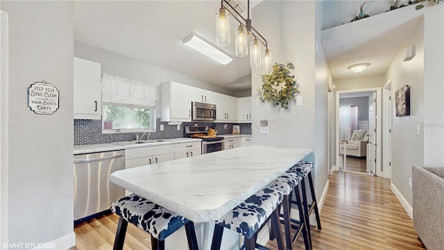 kitchen featuring appliances with stainless steel finishes, decorative backsplash, light countertops, white cabinets, and light wood-style floors