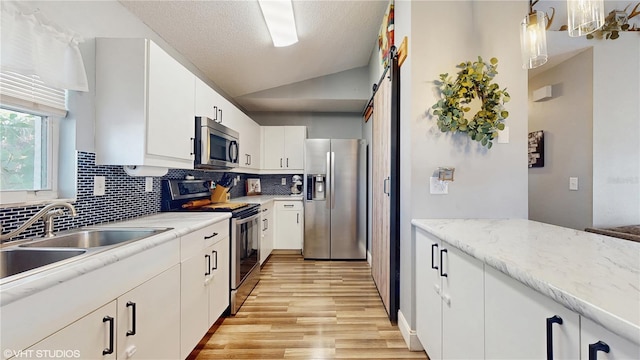 kitchen featuring a sink, lofted ceiling, stainless steel appliances, light wood-style flooring, and decorative backsplash