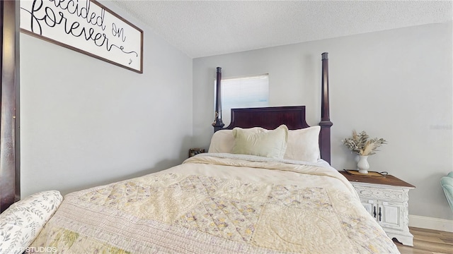 bedroom featuring a textured ceiling, baseboards, and wood finished floors