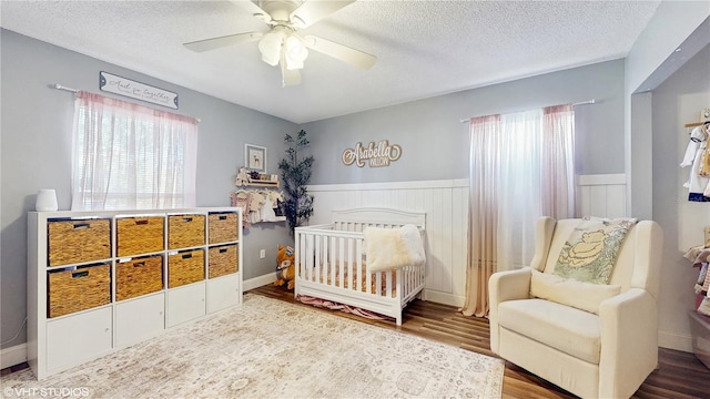 bedroom with wainscoting, a textured ceiling, wood finished floors, and multiple windows