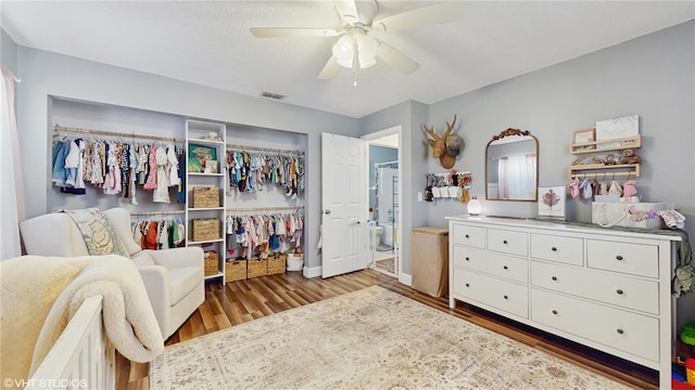 bedroom with a ceiling fan, a closet, ensuite bath, visible vents, and wood finished floors