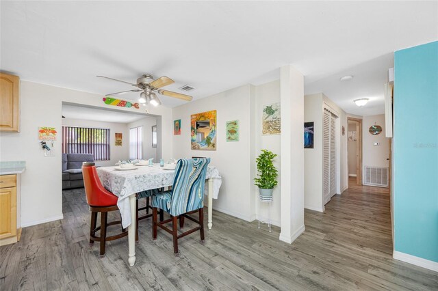 dining space with light wood finished floors, baseboards, visible vents, and ceiling fan