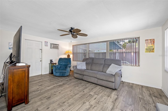 living room with a wall mounted air conditioner, a ceiling fan, baseboards, and wood finished floors