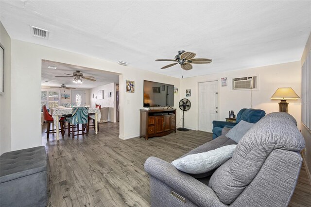 living area featuring a wall mounted air conditioner, a ceiling fan, wood finished floors, baseboards, and visible vents