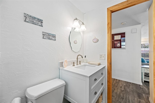 half bath featuring toilet, a textured wall, vanity, and wood finished floors