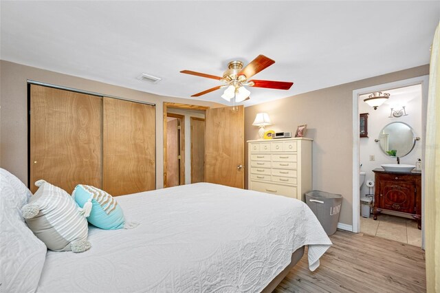 bedroom with a closet, ceiling fan, light wood finished floors, ensuite bath, and visible vents