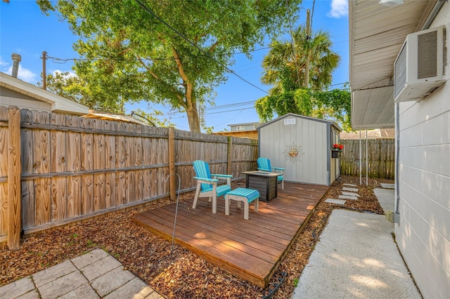 wooden deck with a fenced backyard, an outbuilding, a shed, and a wall unit AC