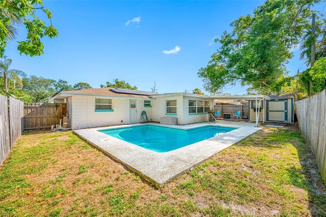 back of property with a storage unit, a fenced in pool, a fenced backyard, a lawn, and roof mounted solar panels