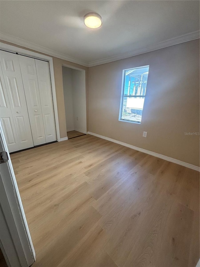 unfurnished bedroom with crown molding, light wood-style floors, baseboards, and a closet