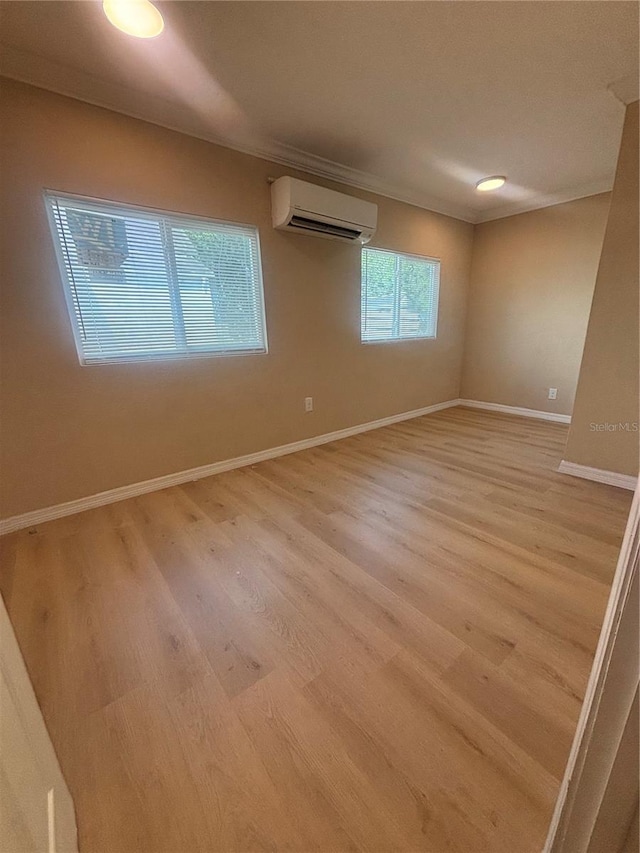 empty room featuring baseboards, a wall mounted air conditioner, and light wood finished floors