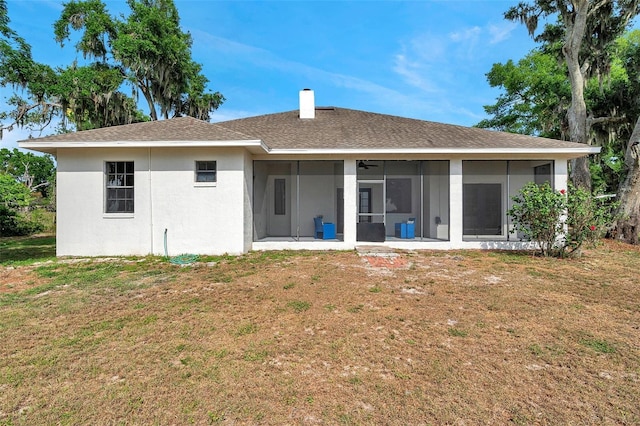 rear view of house featuring a chimney, a sunroom, a yard, and stucco siding