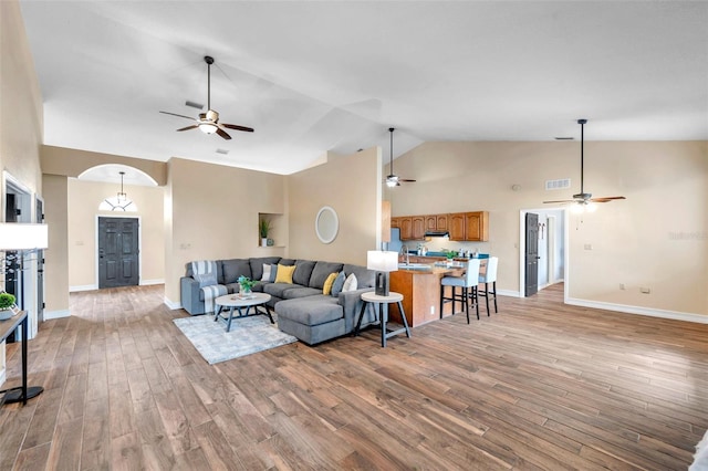 living room with high vaulted ceiling, ceiling fan, arched walkways, and light wood finished floors