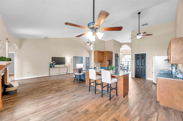 kitchen with brown cabinetry, a ceiling fan, arched walkways, and stainless steel microwave