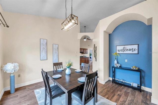 dining room with a ceiling fan, wood finished floors, arched walkways, baseboards, and lofted ceiling
