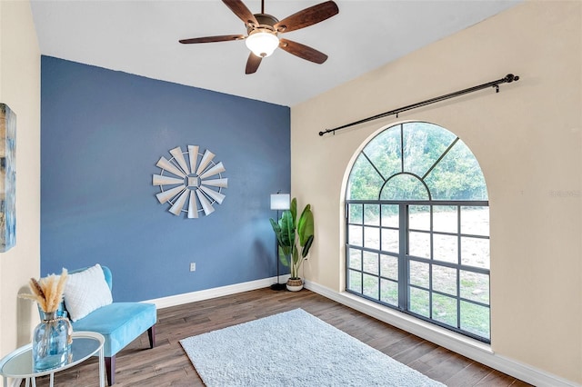 living area featuring wood finished floors, a healthy amount of sunlight, baseboards, and ceiling fan