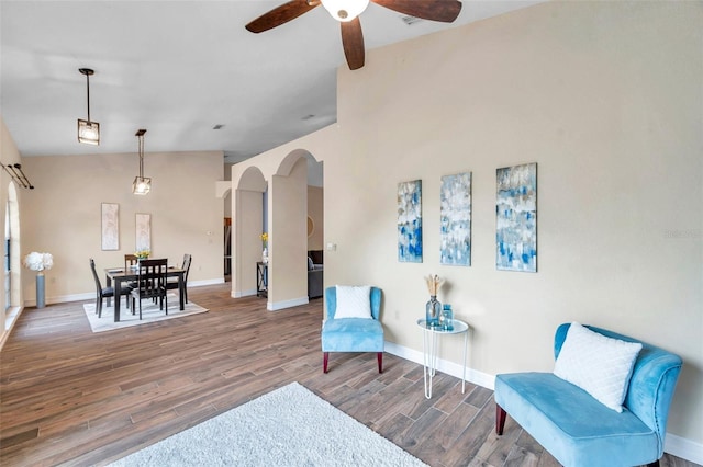sitting room with arched walkways, vaulted ceiling, baseboards, wood finished floors, and ceiling fan