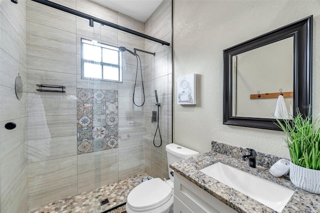 full bath with a textured wall, a tile shower, vanity, and toilet