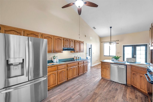 kitchen with brown cabinets, under cabinet range hood, stainless steel appliances, a ceiling fan, and high vaulted ceiling