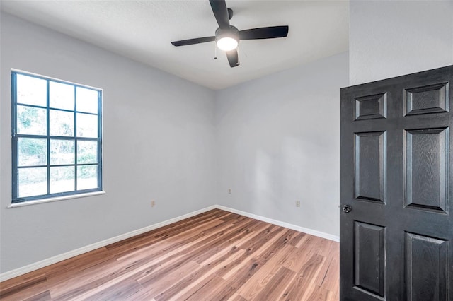 spare room featuring light wood-style flooring, a ceiling fan, and baseboards