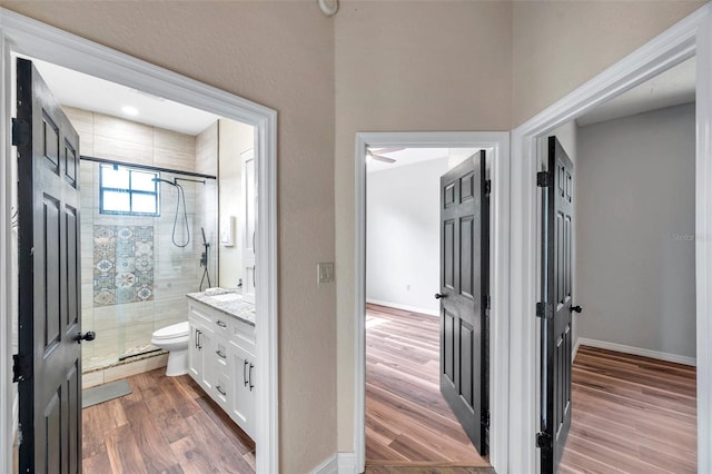 bathroom with toilet, a stall shower, baseboards, wood finished floors, and vanity