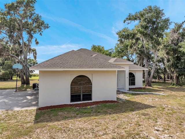 rear view of property with a yard, roof with shingles, and stucco siding