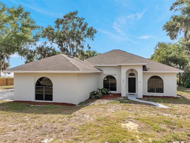 view of front of house with a shingled roof, a front lawn, stucco siding, and fence