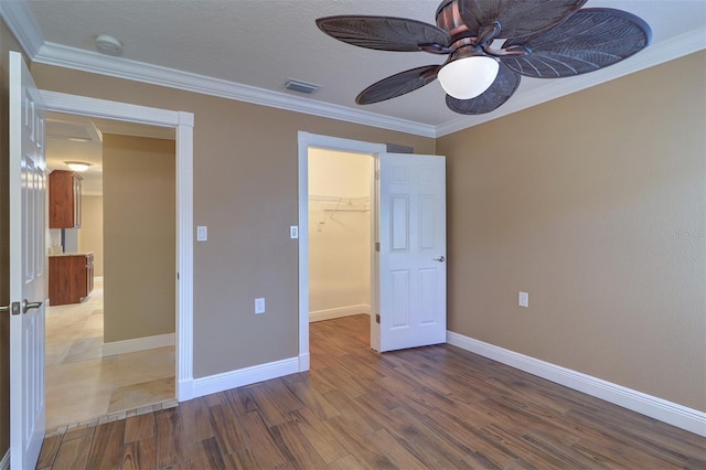 5449 Manatee Point Dr, New Port Richey, FL 34652 - unfurnished bedroom featuring wood finished floors, a walk in closet, ornamental molding, a closet, and a ceiling fan