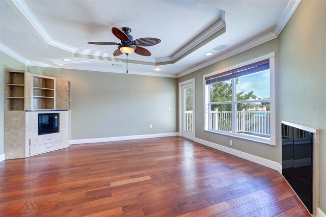 5449 Manatee Point Dr, New Port Richey, FL 34652 - unfurnished living room with a glass covered fireplace, a tray ceiling, crown molding, wood finished floors, and ceiling fan