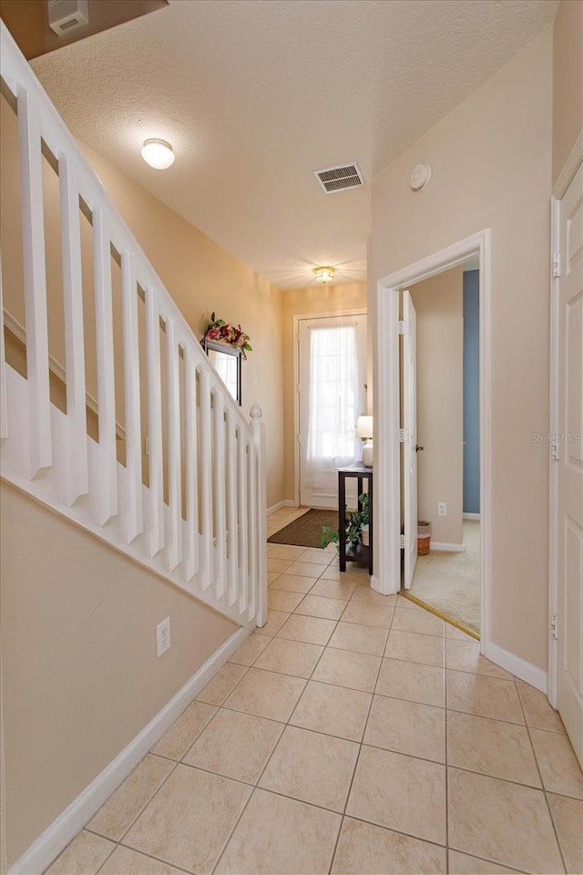 foyer featuring stairway, light tile patterned floors, visible vents, baseboards, and a textured ceiling