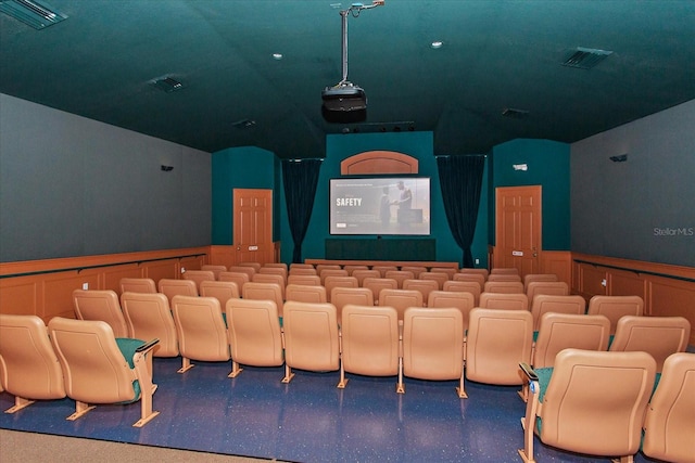 cinema room featuring a wainscoted wall, visible vents, vaulted ceiling, and a decorative wall