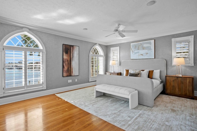 bedroom with crown molding, a textured wall, wood finished floors, and multiple windows