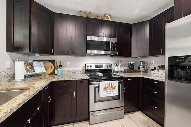 4519 S Grady Ave, Tampa, FL 33611 - kitchen with stainless steel appliances, light stone countertops, light tile patterned flooring, dark brown cabinets, and a textured ceiling