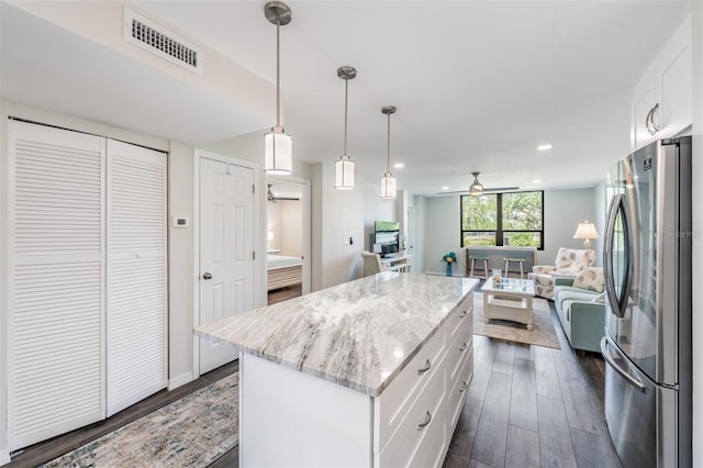 kitchen with open floor plan, freestanding refrigerator, white cabinetry, visible vents, and a kitchen island