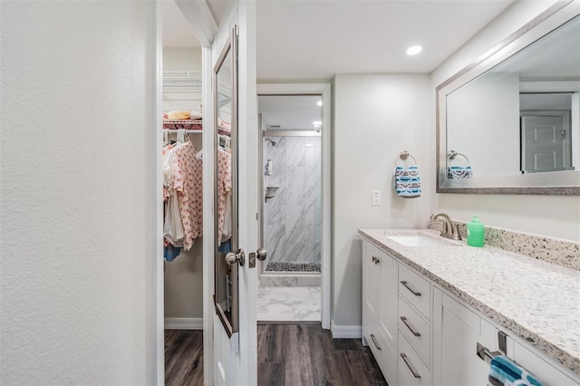 full bath with wood finished floors, a stall shower, a walk in closet, vanity, and baseboards