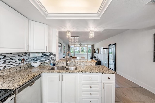 kitchen with white cabinets, a peninsula, stainless steel dishwasher, a sink, and decorative backsplash