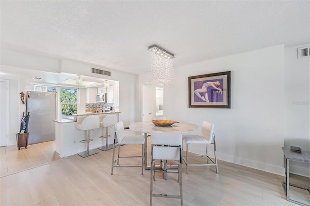 dining space with a chandelier, a textured ceiling, visible vents, and light wood finished floors