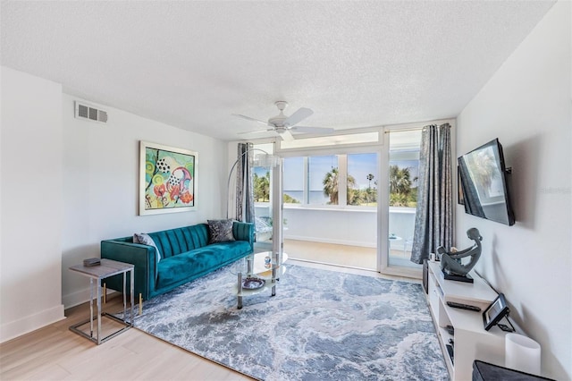 living area featuring a ceiling fan, wood finished floors, a textured ceiling, baseboards, and visible vents