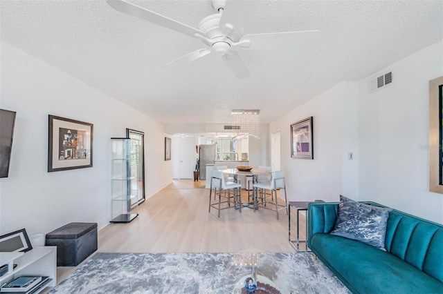 living room featuring ceiling fan, light wood-style floors, visible vents, and a textured ceiling