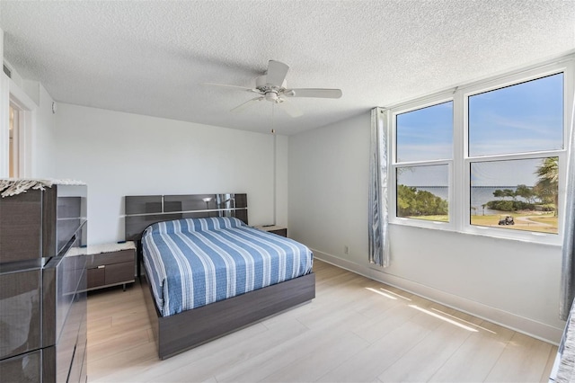 bedroom featuring light wood-type flooring, baseboards, a textured ceiling, and ceiling fan