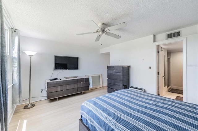 bedroom featuring a ceiling fan, light wood finished floors, a textured ceiling, and visible vents