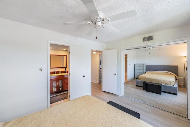 bedroom featuring a sink, a textured ceiling, a closet, light wood-type flooring, and visible vents