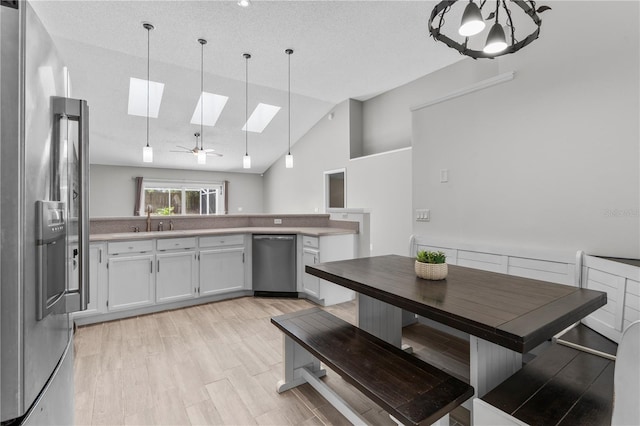 kitchen with vaulted ceiling with skylight, appliances with stainless steel finishes, white cabinetry, and decorative light fixtures