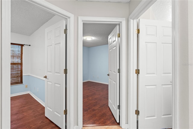 corridor featuring baseboards, dark wood finished floors, and a textured ceiling