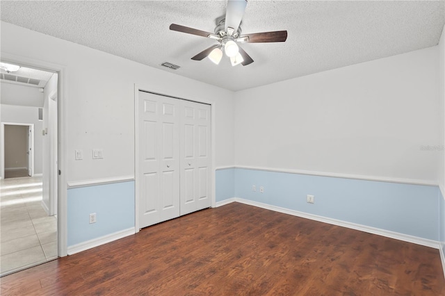 unfurnished bedroom with visible vents, a closet, wood finished floors, a textured ceiling, and a ceiling fan