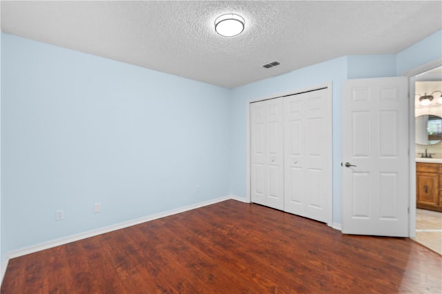 unfurnished bedroom with visible vents, a textured ceiling, baseboards, and dark wood finished floors