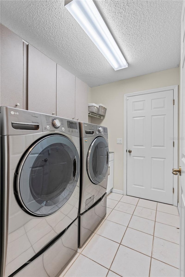 laundry area with separate washer and dryer, a textured ceiling, cabinet space, and light tile patterned floors