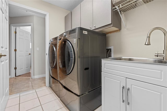 clothes washing area with cabinet space, a sink, light tile patterned floors, baseboards, and separate washer and dryer
