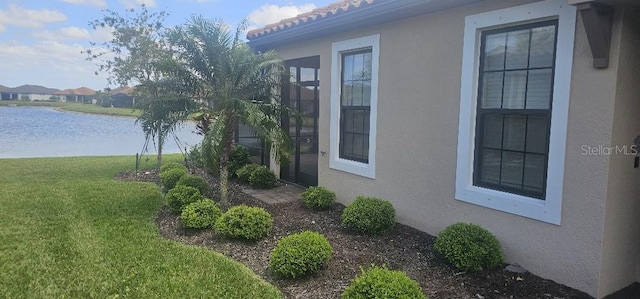view of home's exterior with a lawn, a water view, and stucco siding